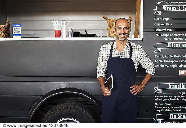 Portrait of confident male owner holding tablet computer while standing against food truck