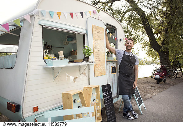Portrait of confident male owner standing outside food truck on street