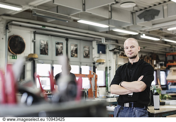 Portrait of confident male teacher standing arms crossed in high school workshop