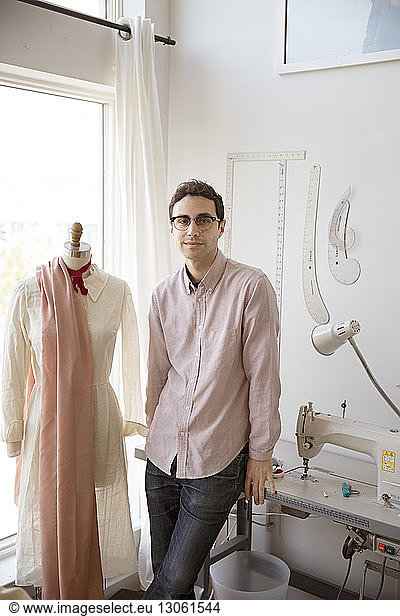 Portrait of confident man standing by dressmaker's model in studio