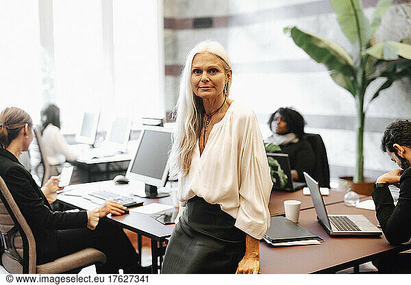 Portrait of confident mature businesswoman leaning on desk in office