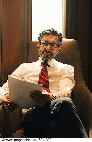 Portrait of confident mature lawyer with documents at legal office