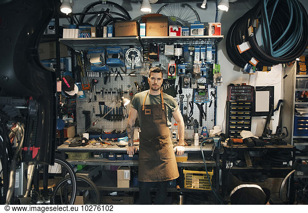 Portrait of confident mechanic leaning on workbench