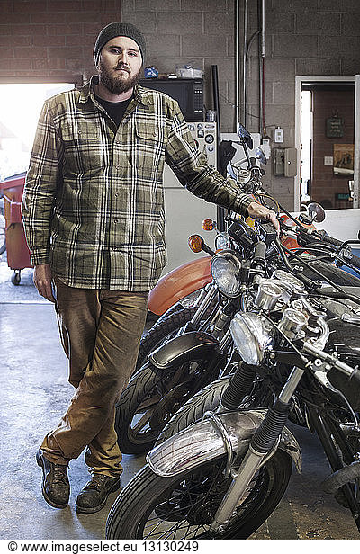 Portrait of confident mechanic standing by motorcycles at auto repair shop