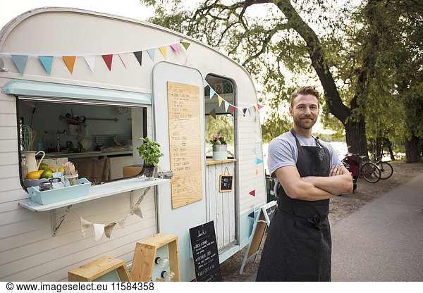 Portrait of confident owner standing arms crossed outside food truck on street