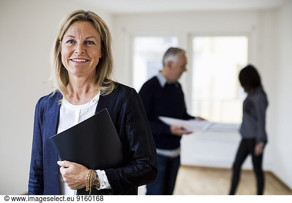 Portrait of confident real estate agent with colleague and woman in background at home