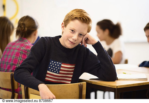 Portrait of confident schoolboy sitting at desk in classroom