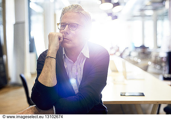 Portrait of confident senior businessman sitting in brightly lit creative office