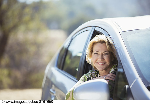 Portrait of confident senior woman leaning out car window