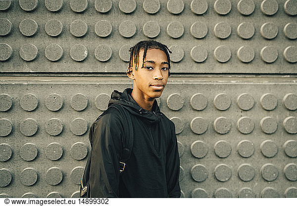 Portrait of confident teenage boy standing against wall