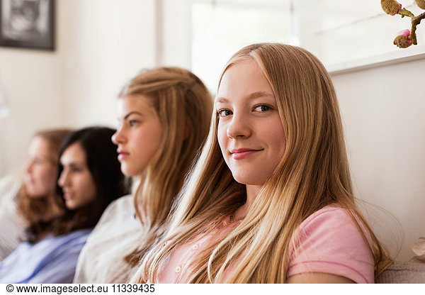 Portrait of confident teenage girl sitting on sofa while friends watching TV at home