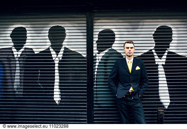 Portrait of confident well-dressed businessman standing against shutter with graffiti