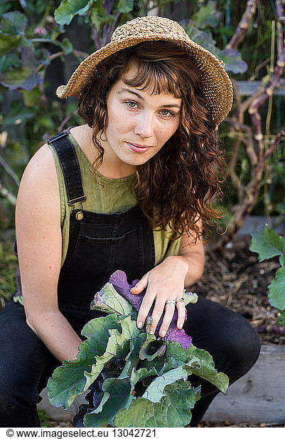 Portrait of confident woman holding leaf vegetables while sitting in garden