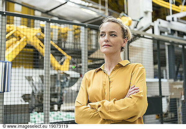 Portrait of confident woman in factory shop floor with industrial robot