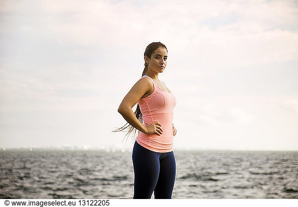 Portrait of confident woman standing against sea and cloudy sky