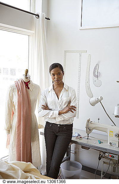 Portrait of confident woman standing by dressmaker's model in studio