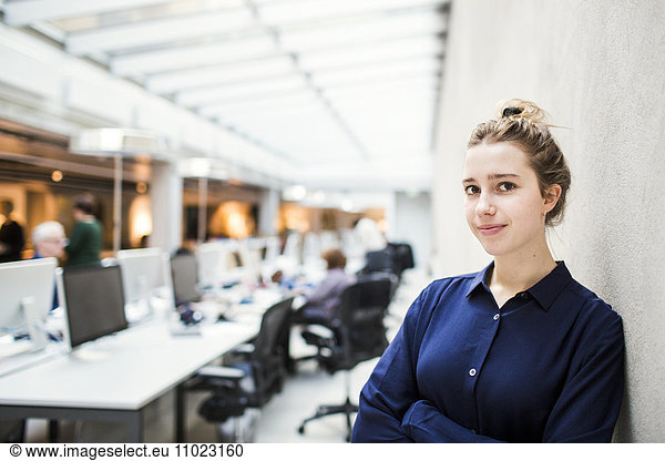 Portrait of confident young businesswoman leaning on wall in office