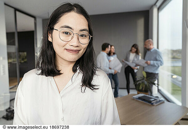 Portrait of confident young businesswoman with colleagues in background in office