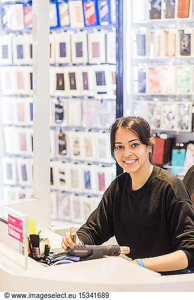 Portrait of confident young female employee smiling while sitting at illuminated desk in store