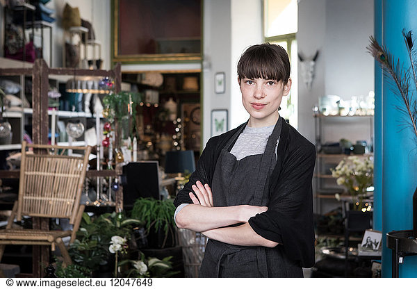 Portrait of confident young female entrepreneur standing with arms crossed at store