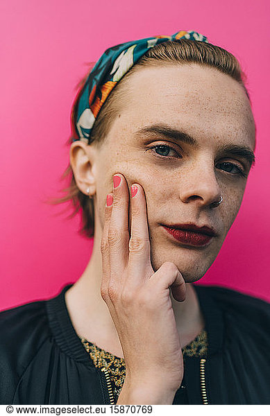 Portrait of confident young man touching cheek while standing against pink background