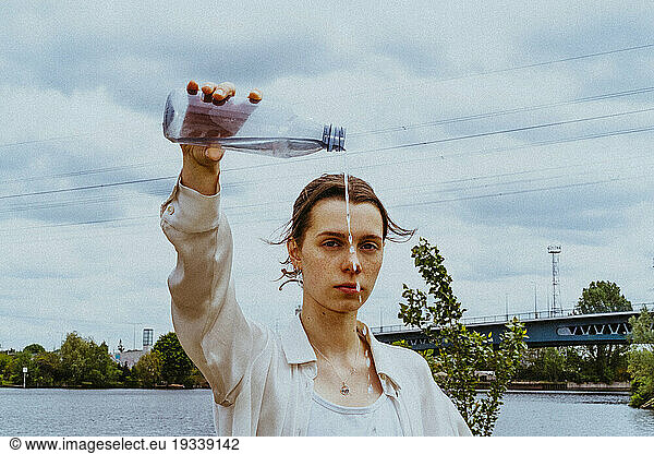 Portrait of confident young non-binary person pouring water from bottle against sky