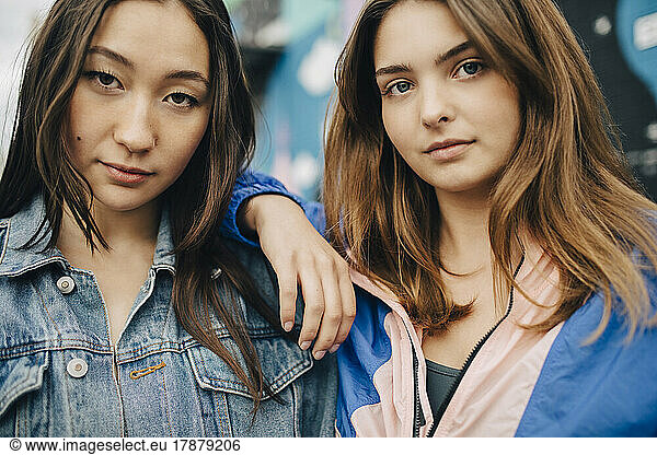 Portrait of confident young woman with hand on shoulder of female friend