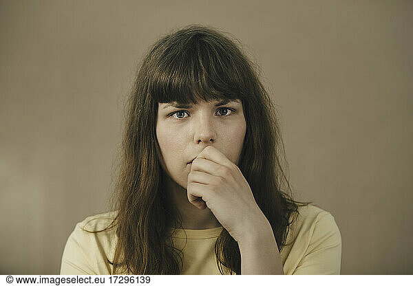 Portrait of confused young woman against beige background