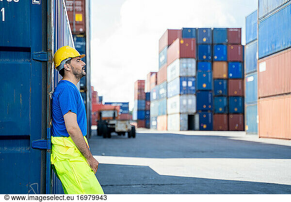 Portrait of container worker leaning on cargo container and look