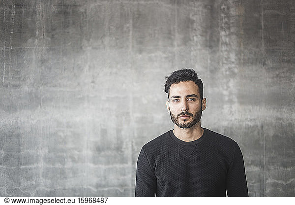 Portrait of contemplating young man standing against gray wall