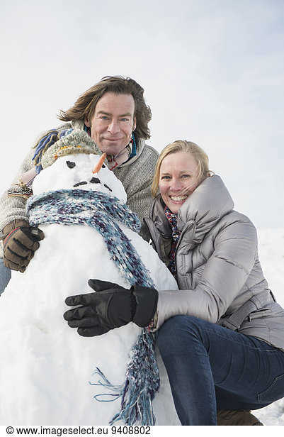Portrait of couple with snowman  smiling
