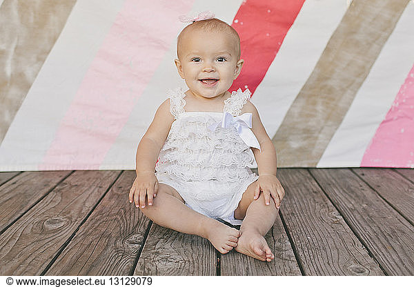 Portrait of cute baby girl sitting on floorboard at birthday party