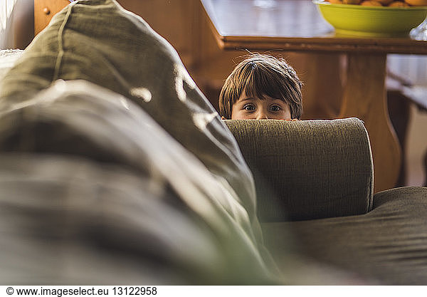 Portrait of cute boy hiding behind sofa at home