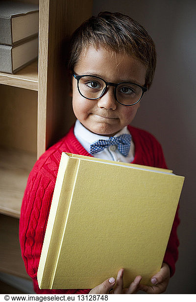 Portrait of cute boy wearing eyeglasses and bow tie while holding book at home