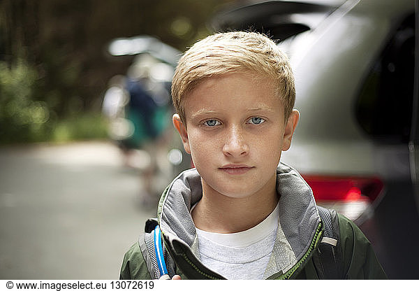 Portrait of cute boy with backpack against car