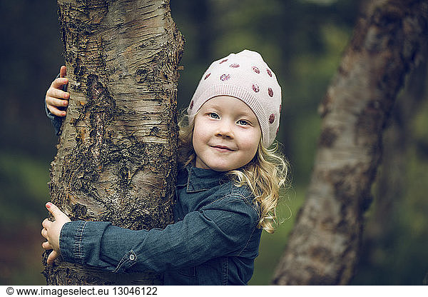 Portrait of cute girl embracing tree trunk at park