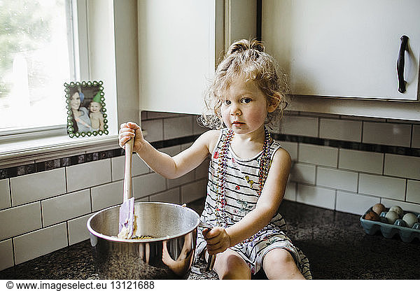Portrait of cute girl preparing food in container while sitting on kitchen counter at home