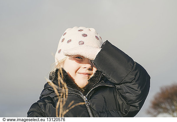 Portrait of cute girl shielding eyes from sunlight while wearing warm clothing