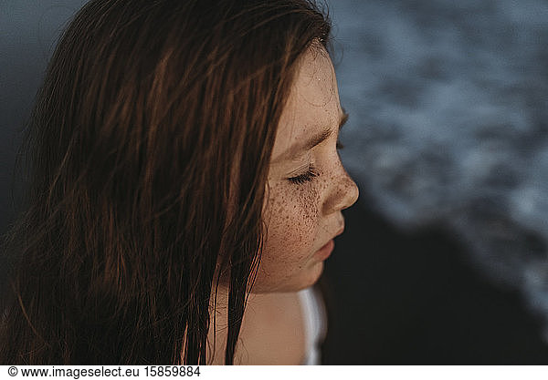 Portrait of cute red headed girl with freckles closing eeditorial in ocean