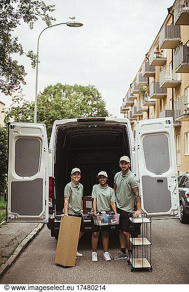 Portrait of delivery coworkers with box and rack against van