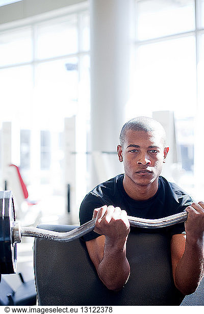 Portrait of determined young man lifting barbell in gym