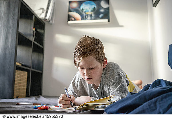 Portrait of drawing boy lying on bed at home