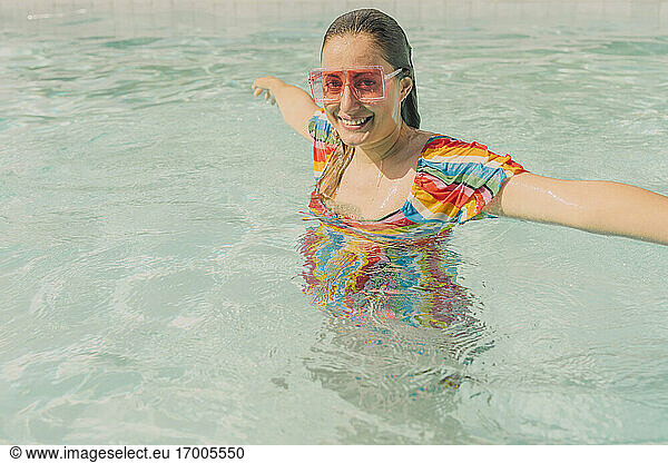 Portrait of dressed woman wearing coloured sunglasses relaxing in swimming pool