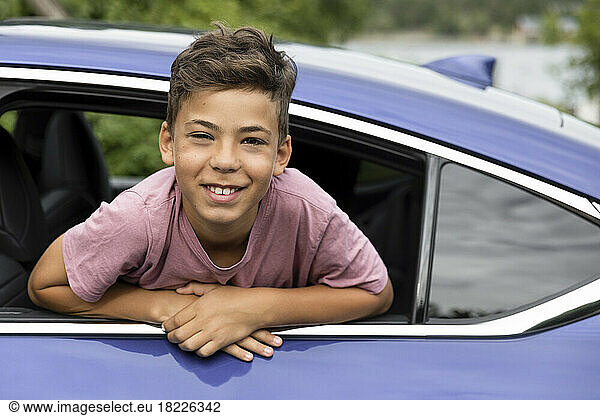 Portrait of excited boy leaning outside through car window