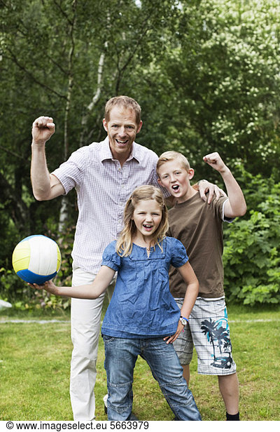 Portrait of excited father and children with soccer ball in back yard