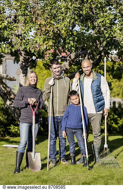 Portrait of family with gardening equipment standing at yard