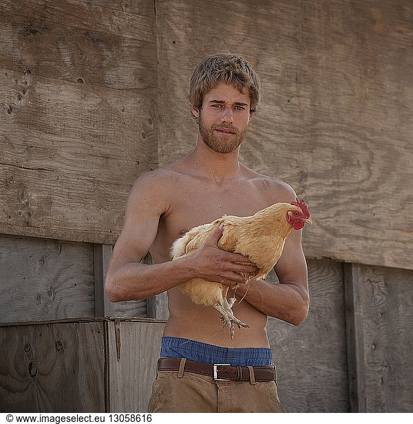 Portrait of farmer carrying chicken against wooden wall