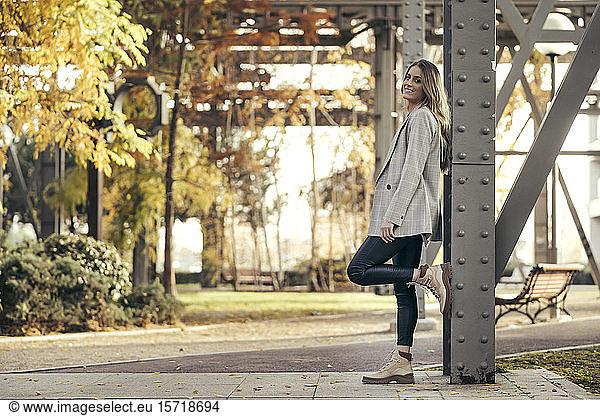 Portrait of fashionable young woman leaning against steel girder in autumn