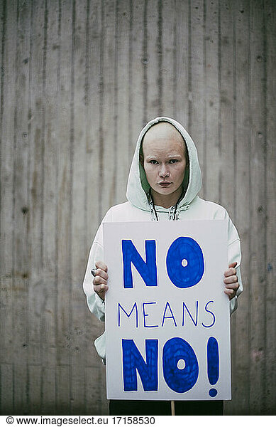 Portrait of female activist holding no means no poster against wall