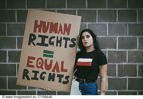 Portrait of female activist with human rights signboard against wall
